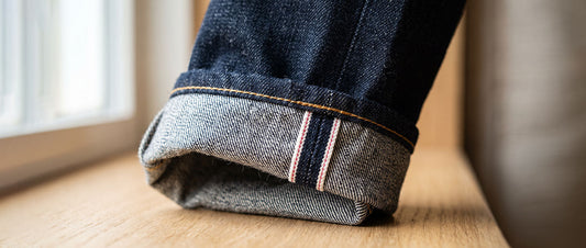 Close-up of cuffed dark indigo selvedge denim jeans showing the classic red selvedge ID and premium denim texture.