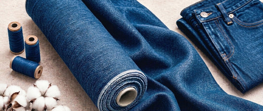 Roll of indigo denim fabric with cotton, thread spools, and folded jeans