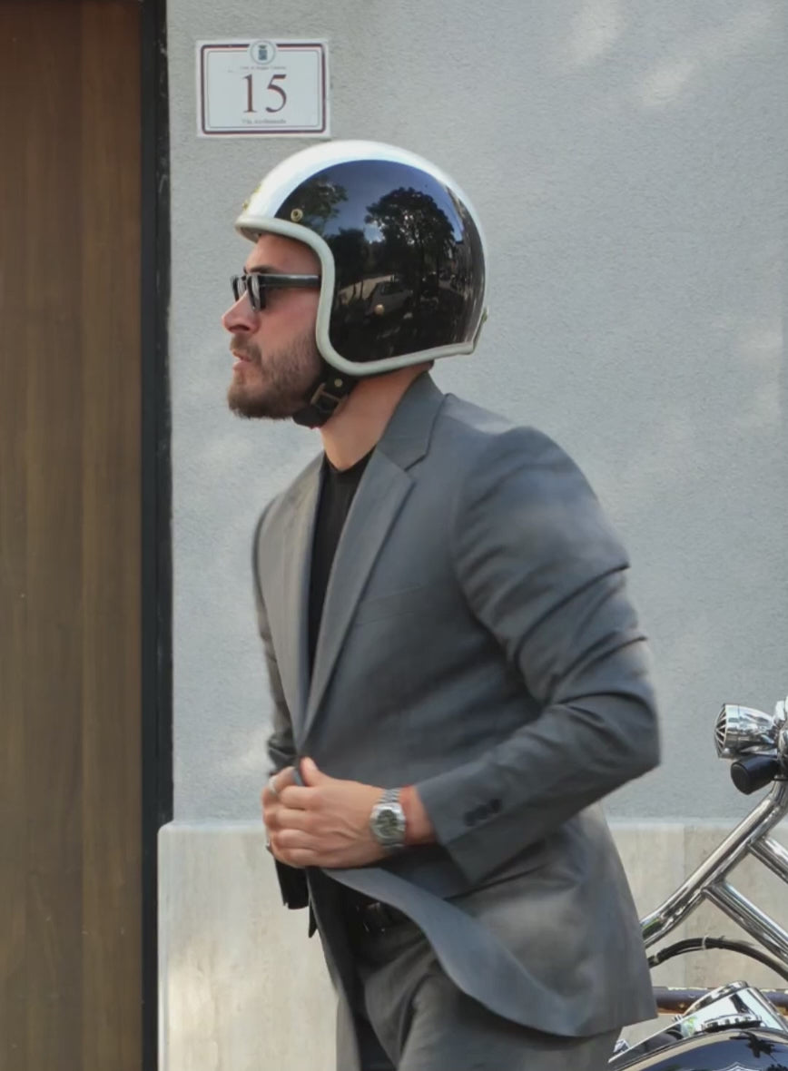 Man in a grey herringbone wool jacket and helmet beside a motorcycle