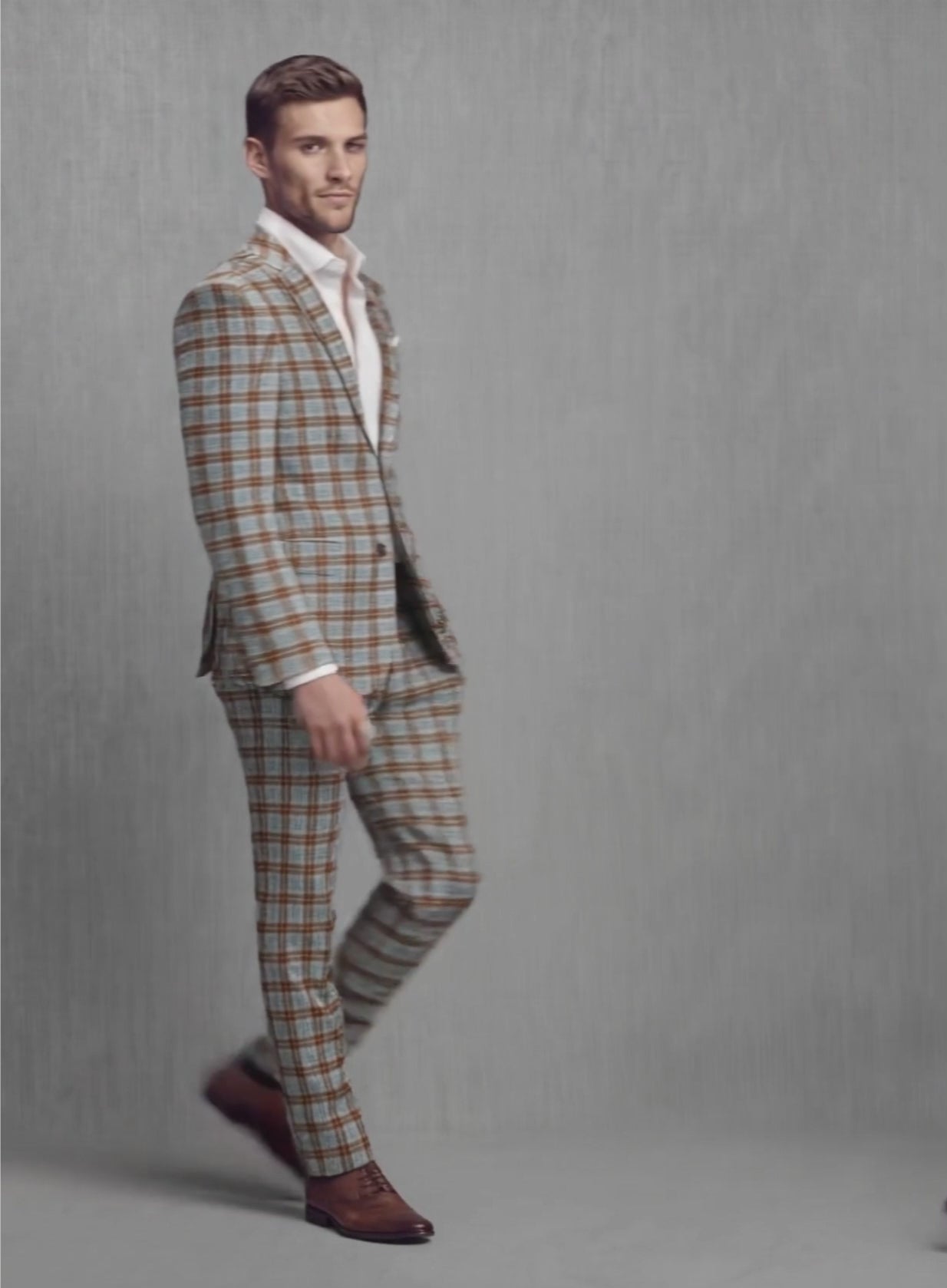 Man walking in a grey check soft tweed suit with brown and blue plaid, side view